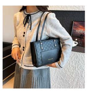 Détail du cuir tressé à damier sur un sac cabas noir porté par un mannequin de mode