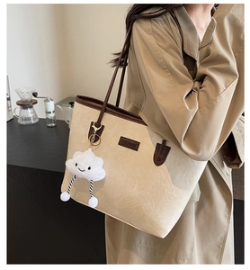 Detail of cream tote bag with brown straps and white cloud pendant worn by a model
