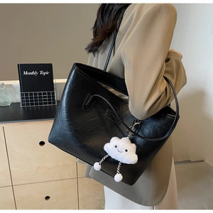 Detail of black faux leather tote with vintage oil-wax texture and plush cloud charm