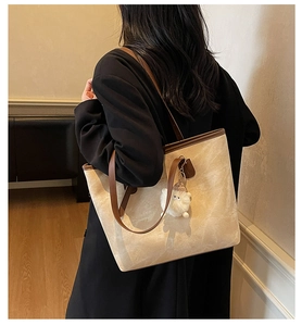 Dettaglio di una borsa tote beige con finiture in pelle marrone e ciondolo peluche