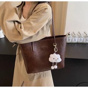 Detailed close-up of a large brown leather tote bag featuring a cute white cloud pendant