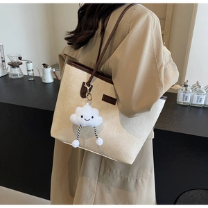 Detail of cream tote bag with contrast brown straps and a soft cloud charm