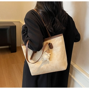 Dettaglio borsa tote beige con tracolla marrone e ciondolo a forma di pecora di peluche