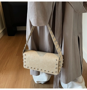 Detailed close-up of beige shoulder bag featuring silver rivets and faux leather texture