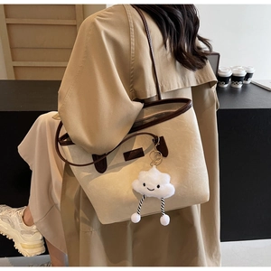 Detail of cream tote bag with litchi texture, dark brown handles, and cloud plush charm