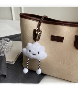 Close-up of white plush cloud keychain with smile embroidery on cream leather tote bag