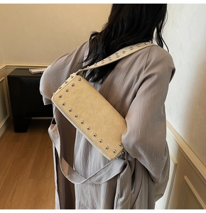 Detail of silver rivets on a beige leather shoulder bag worn by a model in a minimal room