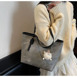 Dettaglio di una grande borsa tote grigia con manici in pelle e ciondolo a mostro morbido