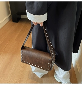 Detail of dark brown leather shoulder bag featuring silver rivets and punk style accents