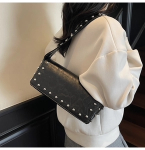 Detail of black rectangular shoulder bag with silver studs worn by model from behind