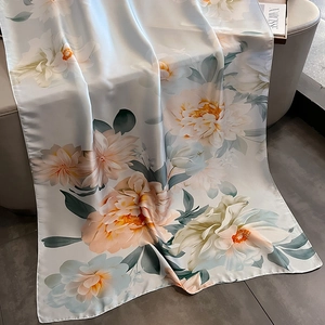 Elegant floral print silk scarf in beige with peony patterns displayed on leather sofa