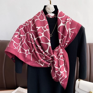 Close-up of elegant red silk scarf with white geometric patterns draped on black knitwear