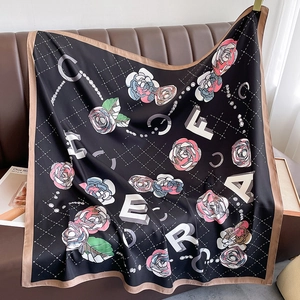 Detailed shot of black silk square scarf featuring pink floral print on a leather surface