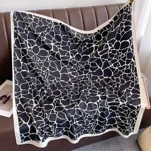 Detail of a large black and white patterned satin square scarf draped on a leather sofa