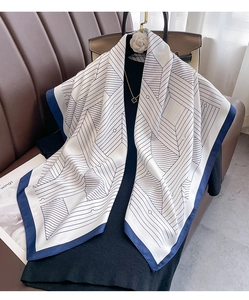 Close-up of white silk scarf with geometric black lines and navy blue border detail