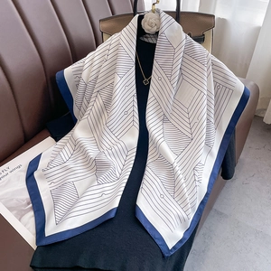 Detail of navy geometric silk scarf draped elegantly next to a designer handbag
