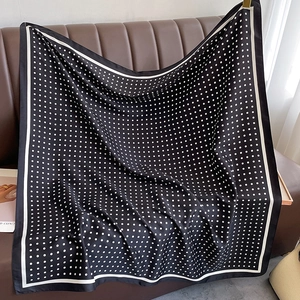 Close-up of elegant black silk scarf with white polka dots on a brown leather surface