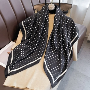 Elegant black and white polka dot silk scarf draped over a beige knit top for a stylish look
