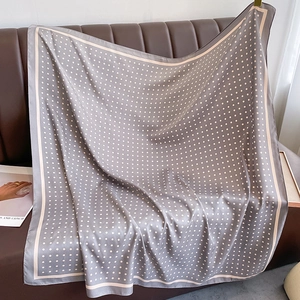 Detail of grey satin scarf with pink polka dots draped on a dark leather sofa
