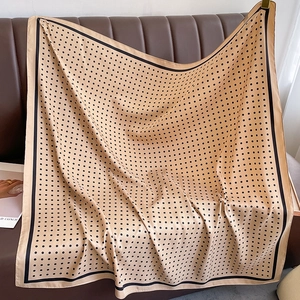 Close-up of beige polka dot silk scarf draped on a leather sofa with elegant texture