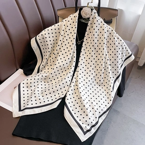 Detail of polka dot silk scarf draped over black knitwear with elegant accessories