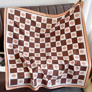 Brown and white checkered silk scarf with orange logos and pink hem on leather sofa