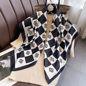 Checkered silk square scarf with geometric pattern draped over a beige knit top