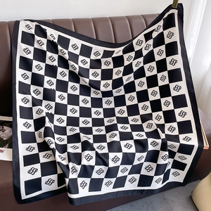 Macro detail of black and white checkerboard silk scarf with SS logo on leather surface