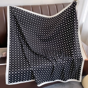 Black and white polka dot silk scarf with letter print draped on a leather sofa