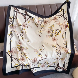 Elegant satin square scarf with magnolia flower print and black contrast borders on sofa