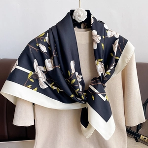 Detail of silk-like scarf with white magnolia print on black background and cream border