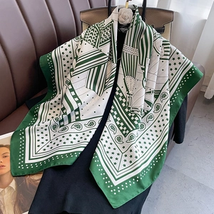 Carré de soie 90cm à motif paisley vert et détails équestres sur un canapé en cuir