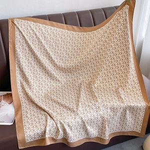 Carré en soie à motifs géométriques et bordures camel sur un canapé en cuir brun
