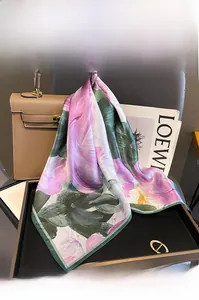 Detail of luxury mulberry silk square scarf with floral pattern tied to a leather handbag