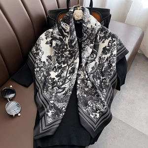 Elegant black and white landscape print silk shawl draped on a leather sofa with fashion props