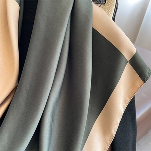 Elegant color block silk scarf in green and beige draped on leather handbag