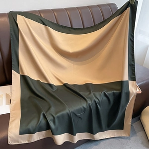 Green and champagne gold geometric silk scarf draped elegantly on a leather sofa