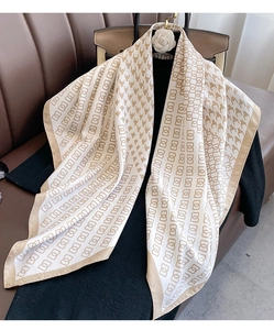 Detail of elegant houndstooth silk scarf draped on a leather sofa with luxury bag