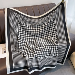 Classic houndstooth twill scarf with contrast black border draped on leather sofa