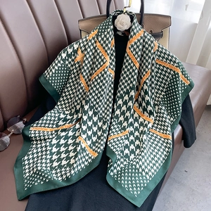 Detail of green and white houndstooth scarf with orange fashion logo strap detail