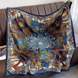 Close-up of a 90cm twill silk scarf with exotic floral palm prints on a leather sofa