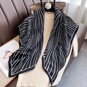 Detail of silk twill scarf with black and white stripes draped on a beige sweater