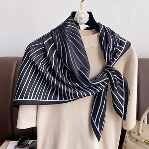 Elegant black and white striped silk square scarf worn over a beige knit sweater