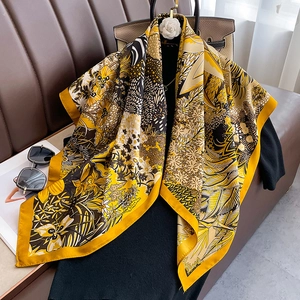 Elegant silk scarf with yellow floral and tropical leaf prints on a leather handbag