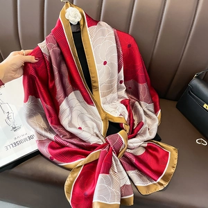 Elegant floral silk scarf with red flower patterns and gold trim draped on a mannequin