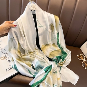 Elegant white silk scarf with lotus floral print draped over a brown leather sofa