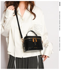 Detail of black glossy leather box bag featuring gold hardware and logo hangtag detail