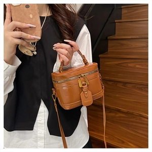 Detail of brown box bag with leather tag, dual zippers, and adjustable shoulder strap