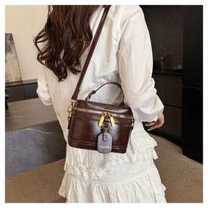 Detail view of vintage dark brown leather box bag with gold double zippers and charm