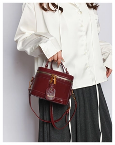 Detail of burgundy glossy box bag with gold double zippers and elegant top handle